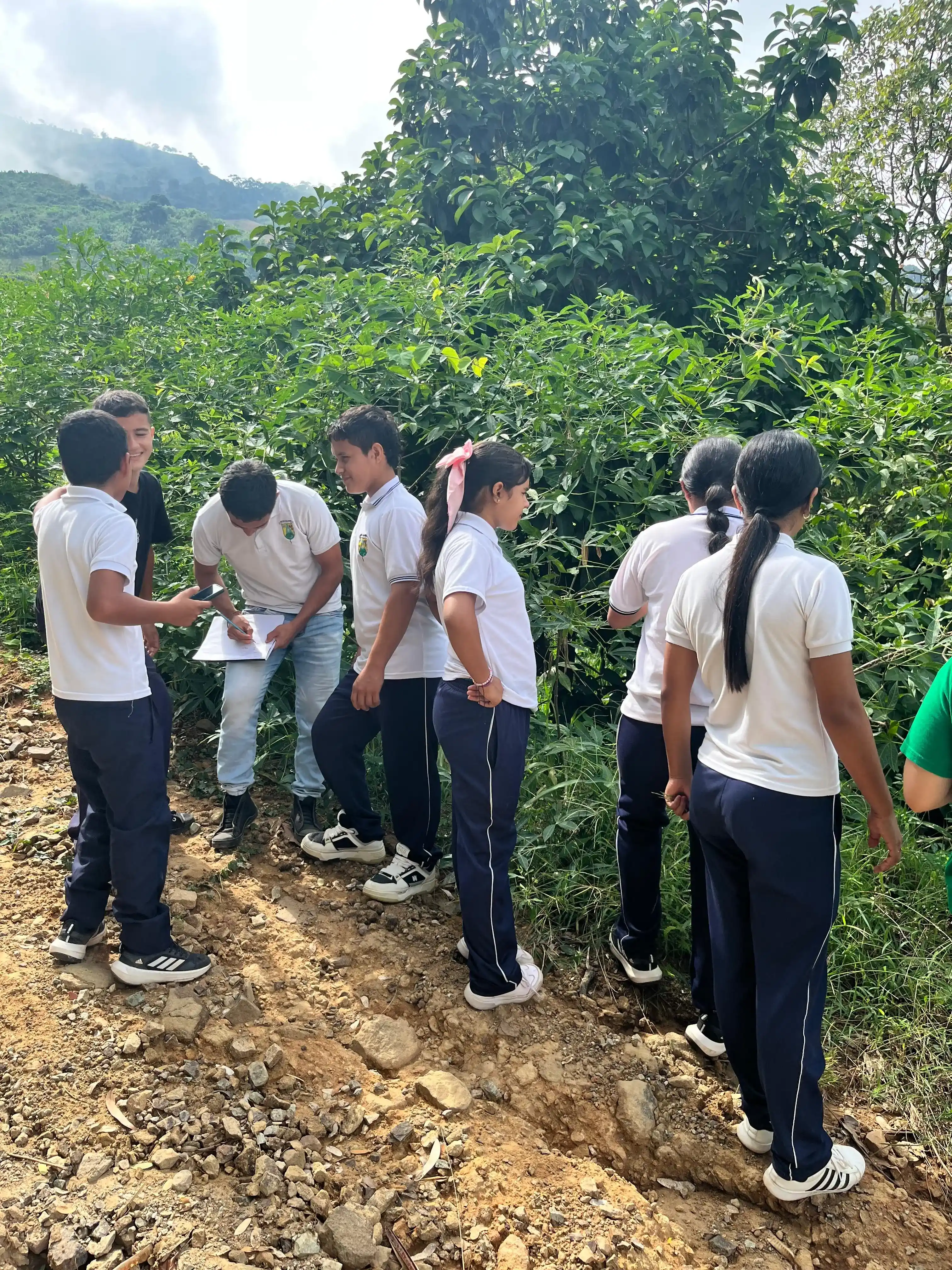 Grupo escolar en uniforme observando vegetación en un camino de tierra entre cerros